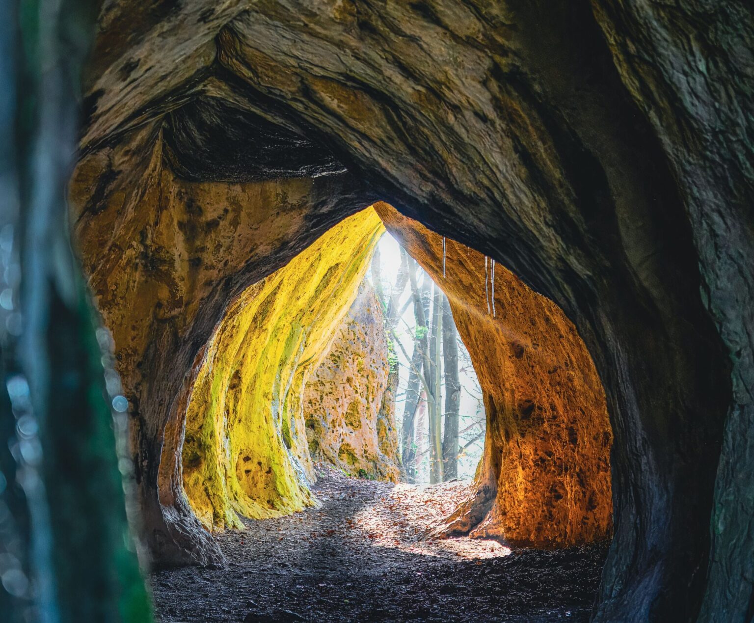 A dramatic view through a cave entrance with sunlight illuminating the path ahead.